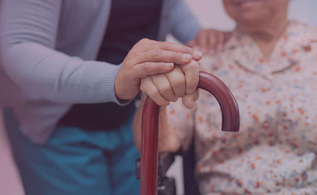 A clinician rests her hand upon an elderly woman's hand grasping a cane.